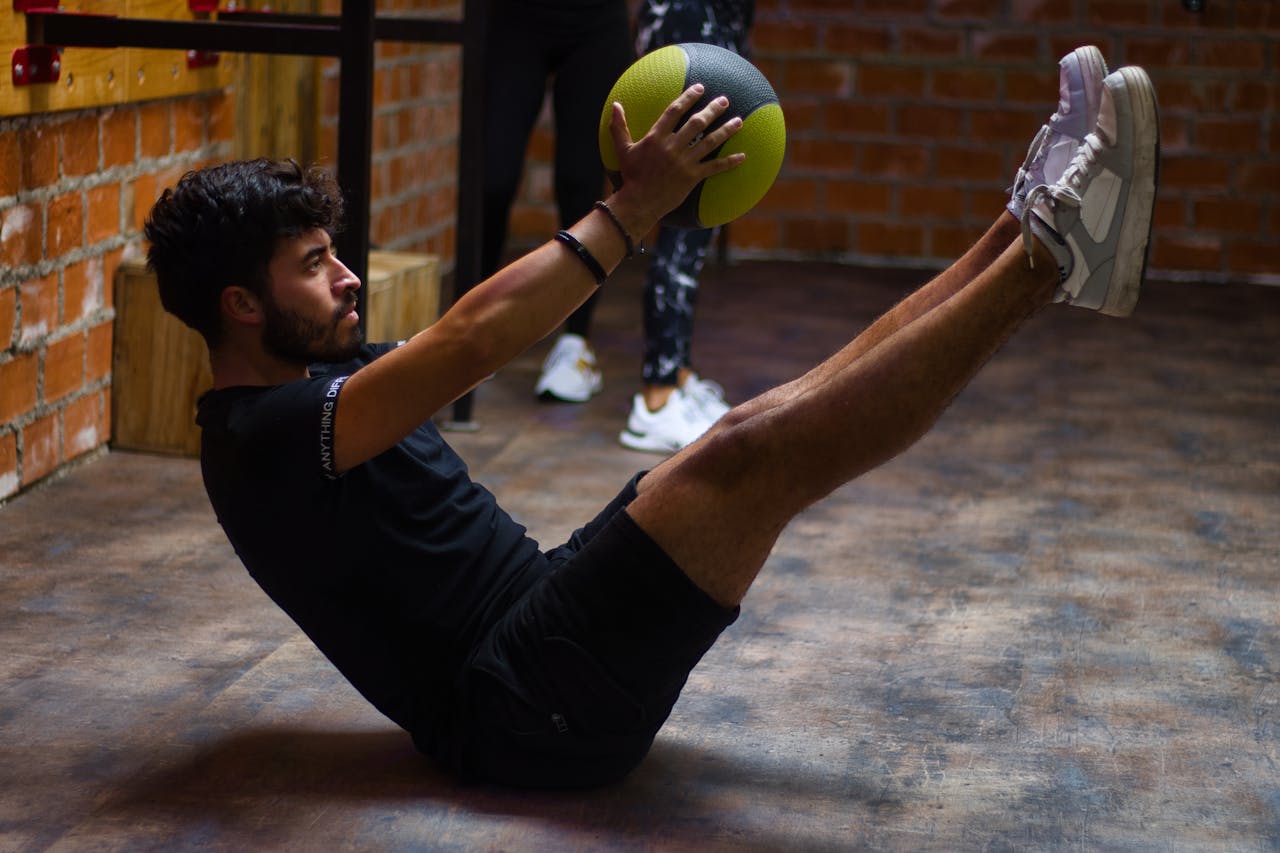 why-choose-us Focused man performing core exercises with a medicine ball in an indoor gym highlighting fitness and strength.